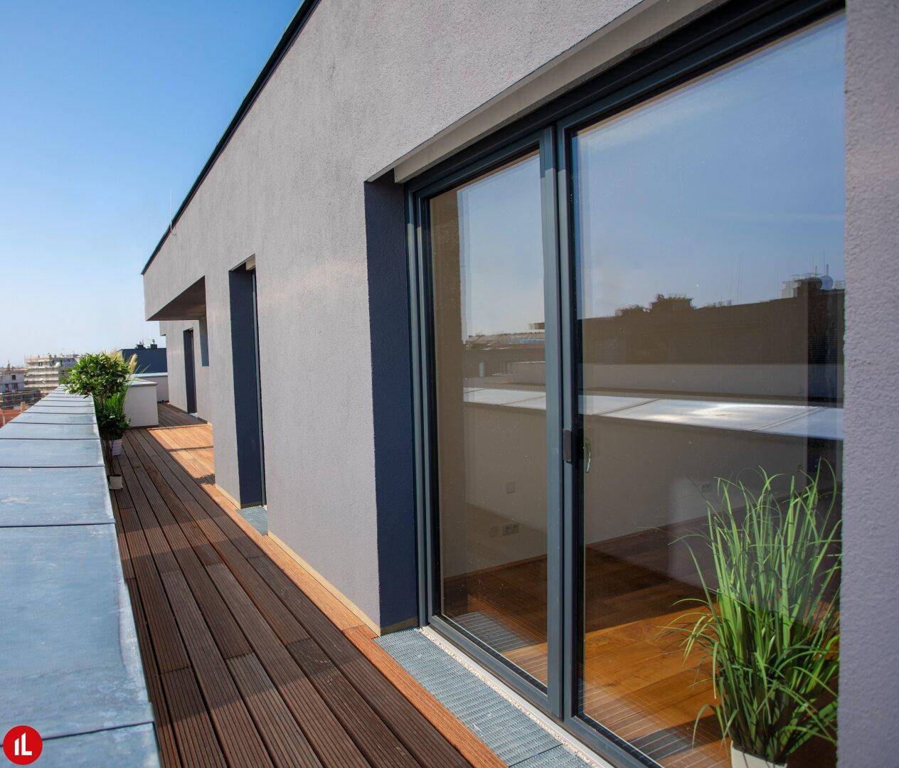 Lange Terrasse mit Holzdielen und großen Schiebetüren zur Wohnung.