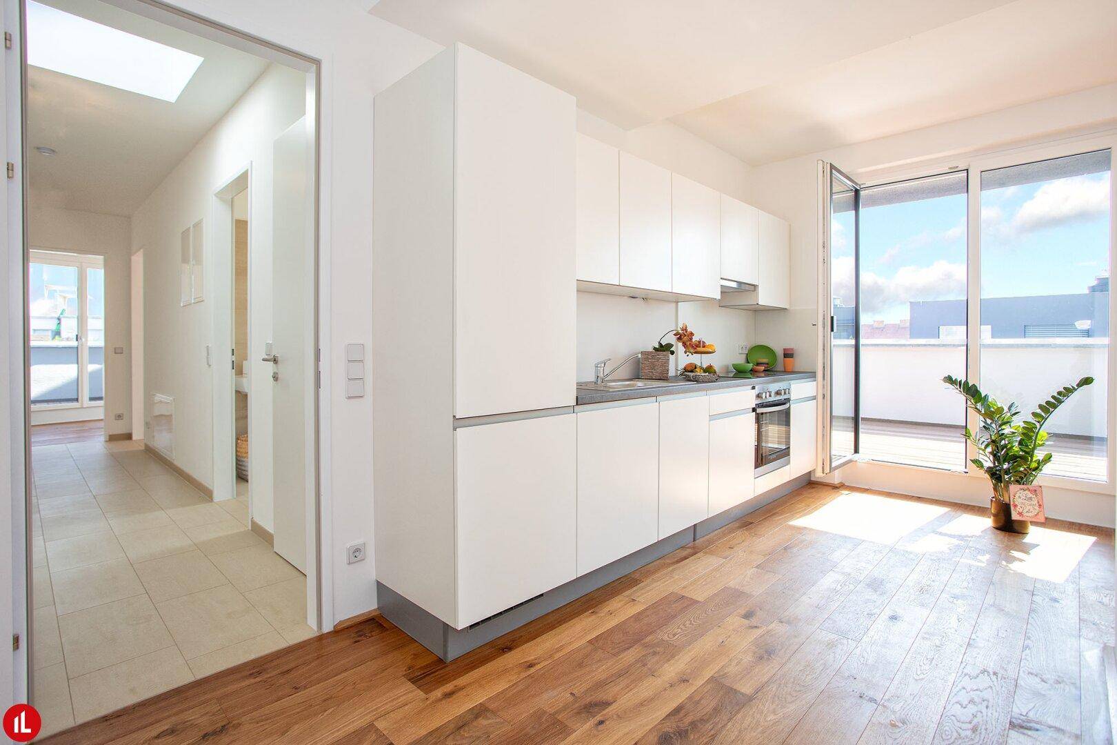 Moderne weiße Einbauküche mit Holzboden und Zugang zur Terrasse.