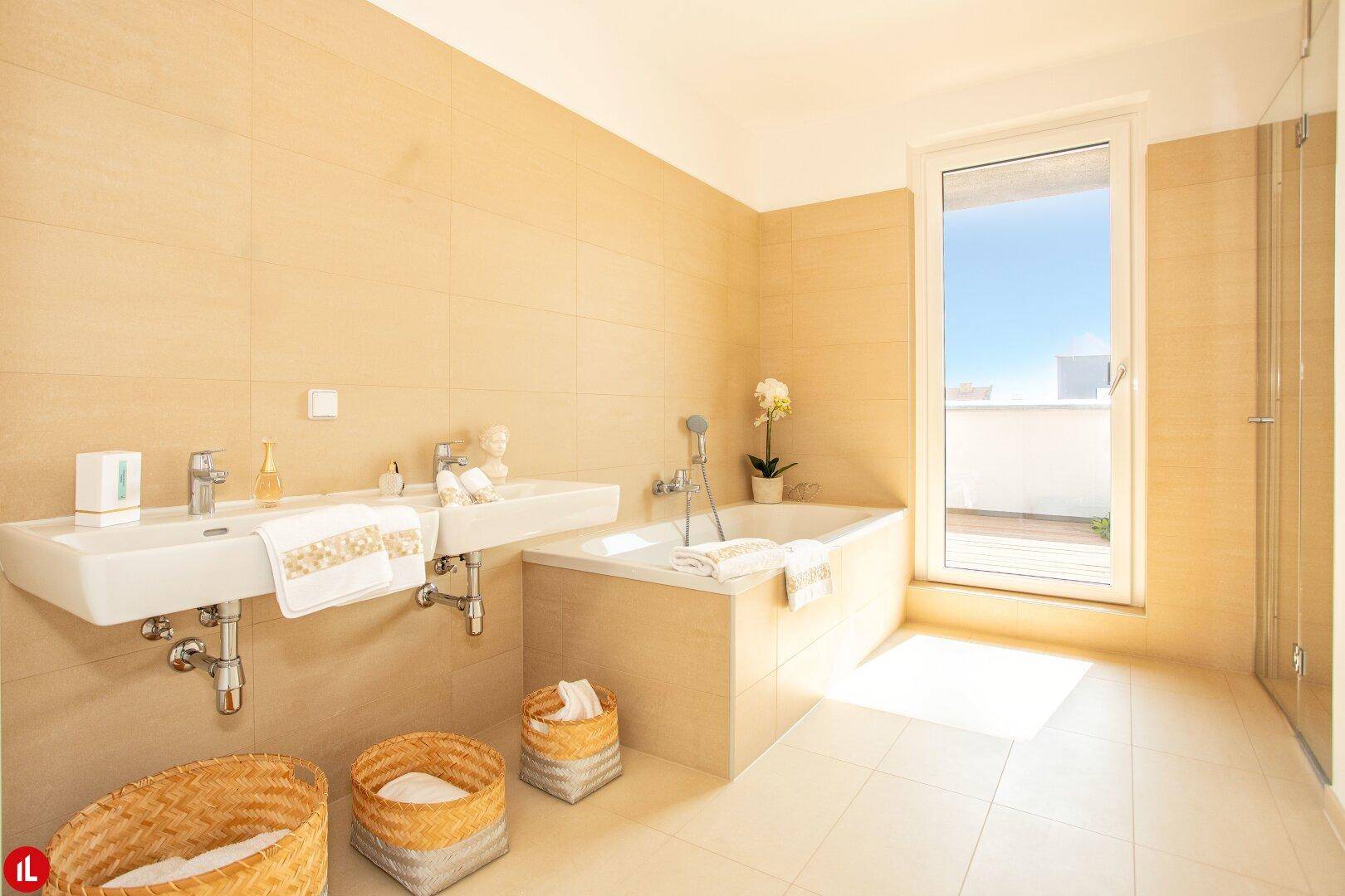 Helles Badezimmer mit beigefarbenen Fliesen, Doppelwaschbecken und Badewanne.
