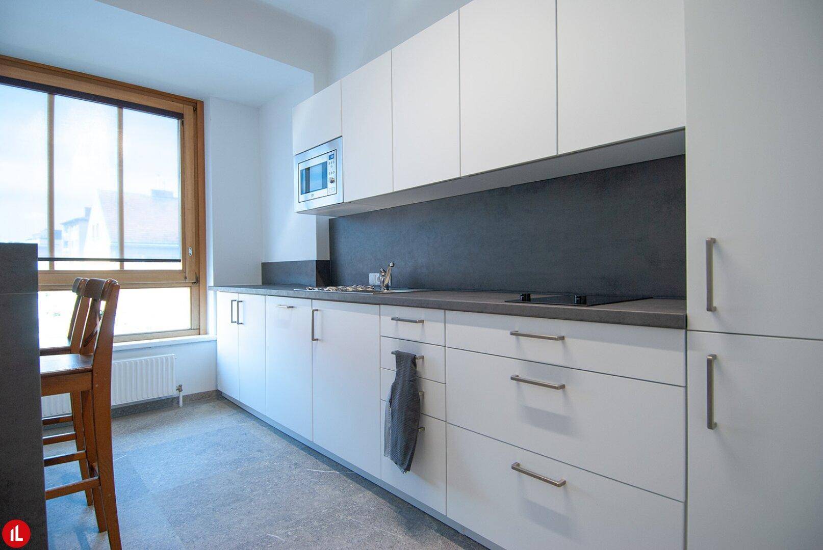 Moderne Küche mit weißen Schränken, dunkler Arbeitsplatte, integrierten Geräten und Fliesenboden.