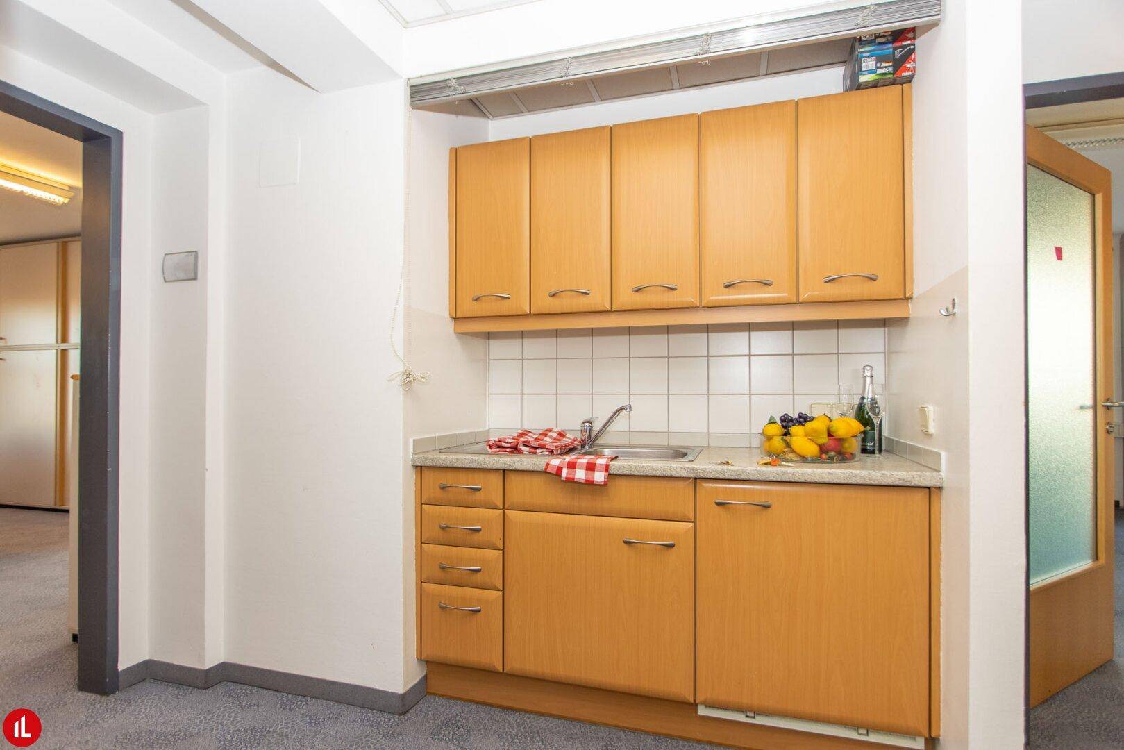 Kleine Küchenzeile mit Holzschränken, Spüle und Fliesenrückwand, ideal für eine schnelle Zubereitung.