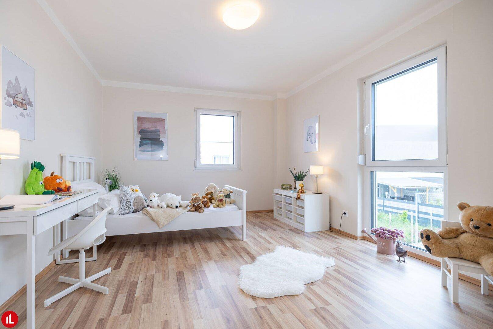 Helles Kinderzimmer mit Holzboden, Schreibtisch und großen Fenstern für viel Tageslicht.