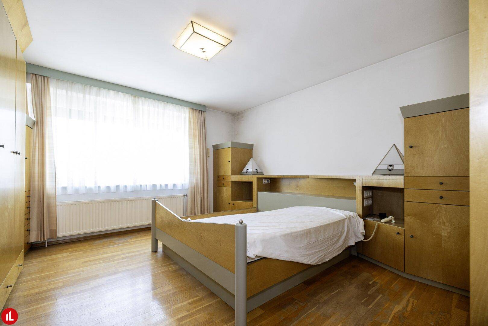 Helles Schlafzimmer mit Holzparkettboden, Einbauschränken und einem großen Fenster für viel Tageslicht.