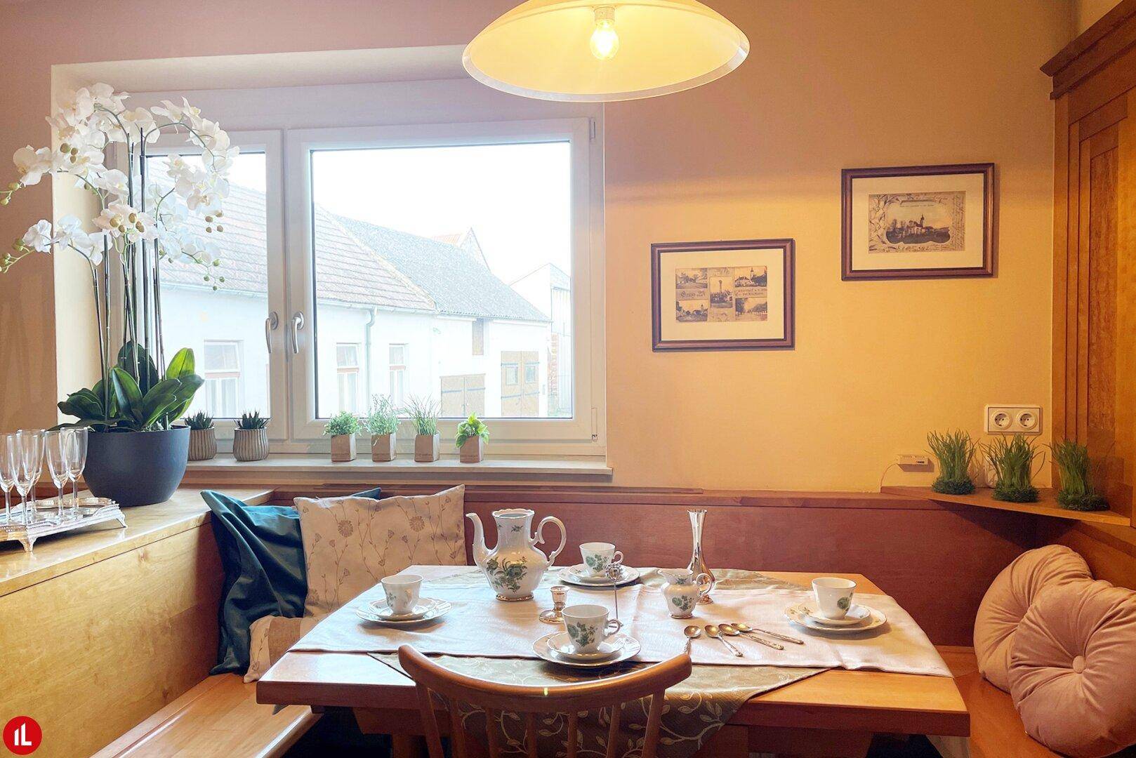 Gemütlicher Essbereich mit Holztisch, Eckbank und Blick auf die Nachbarschaft durch das Fenster.