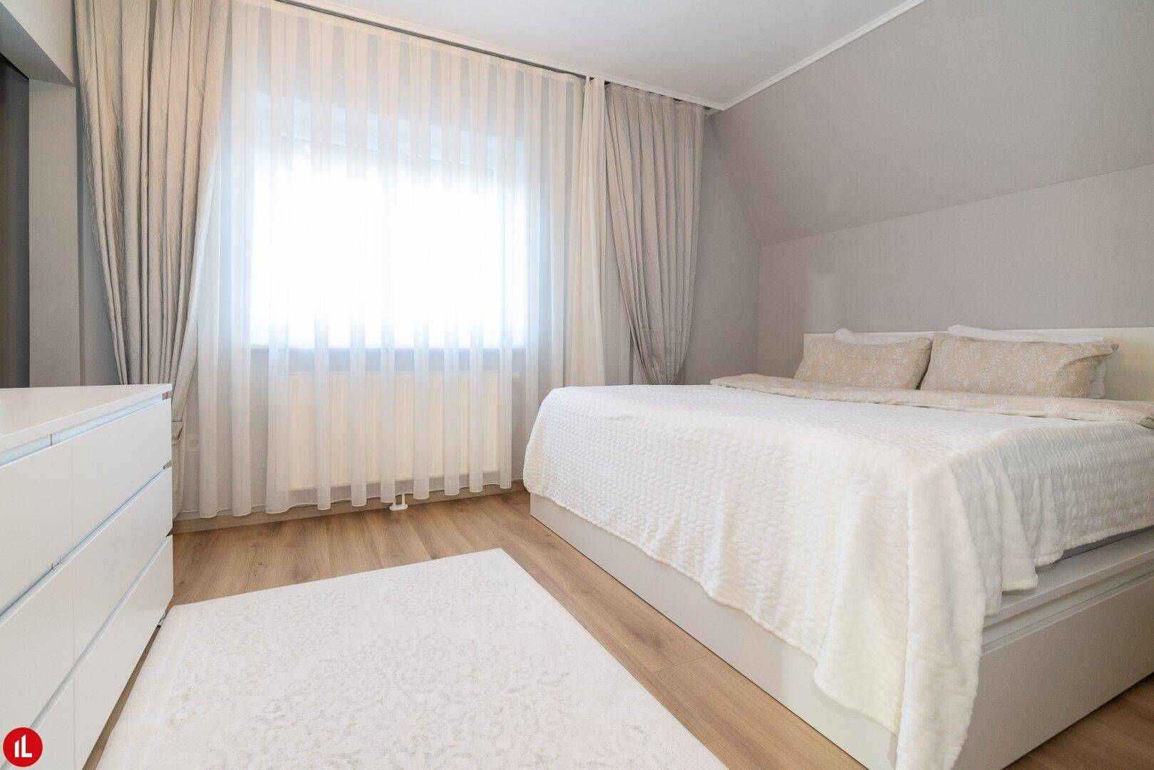Helles Schlafzimmer mit großem Doppelbett, weißer Kommode und Holzboden.