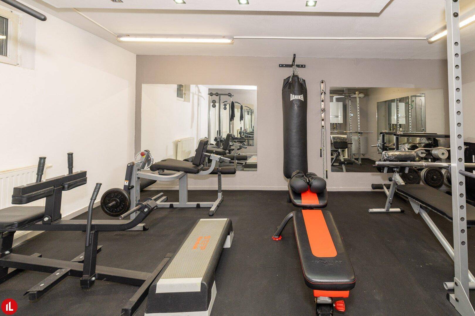 Gut ausgestatteter Fitnessraum mit verschiedenen Trainingsgeräten und Spiegelflächen.