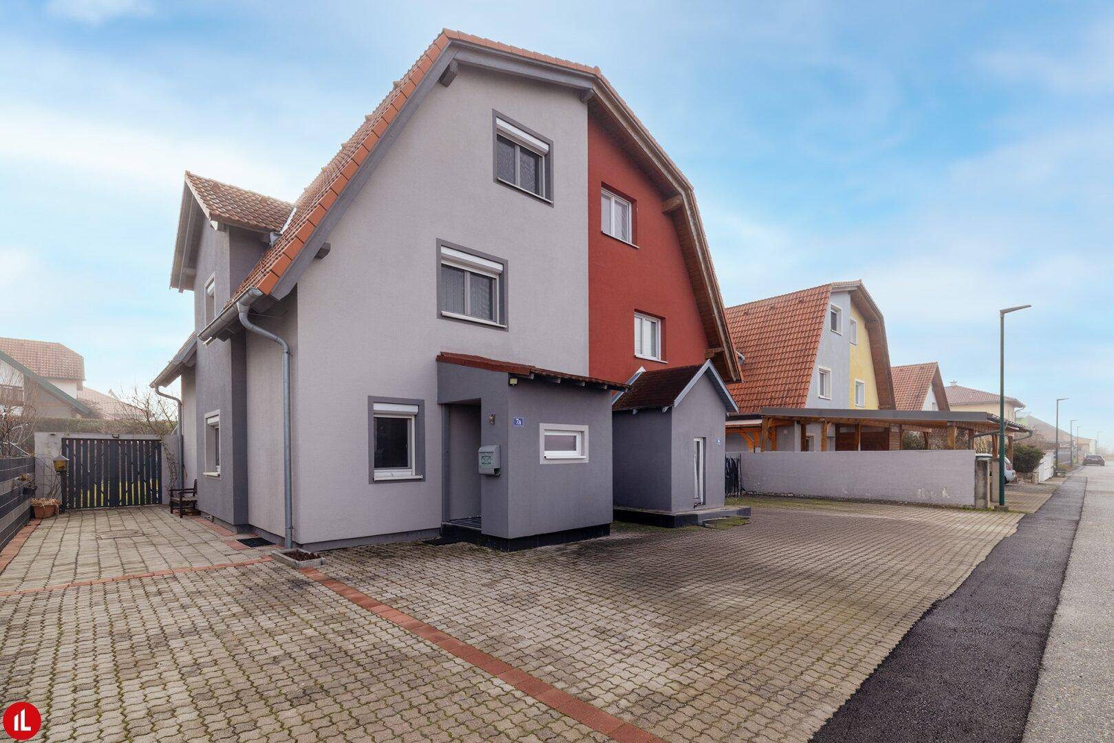 Modernes Einfamilienhaus mit grauer und roter Fassade und gepflasterter Auffahrt.