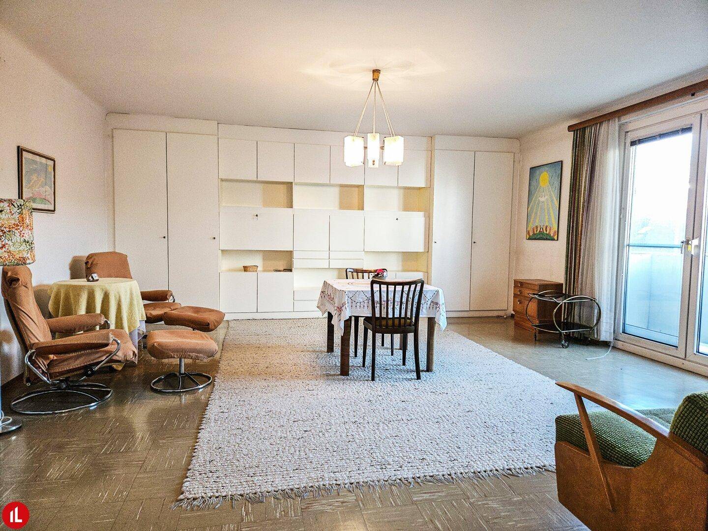 Geräumiger Wohn-Essbereich mit Teppich, Einbauschränken und Zugang zum Balkon.