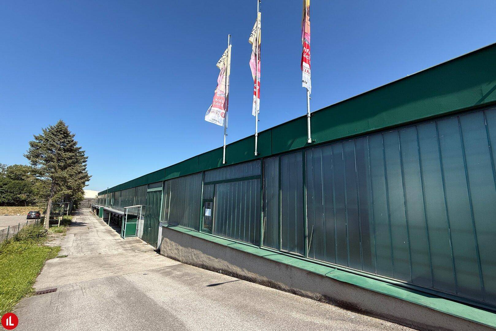Außenansicht eines modernen Geschäftsgebäudes mit großen Glasflächen und Fahnenmasten unter blauem Himmel.