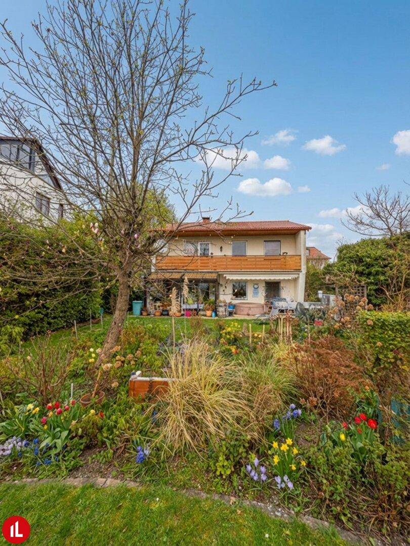 Rückseite eines traditionellen Hauses mit einem farbenfrohen, blühenden Garten und Terrasse.