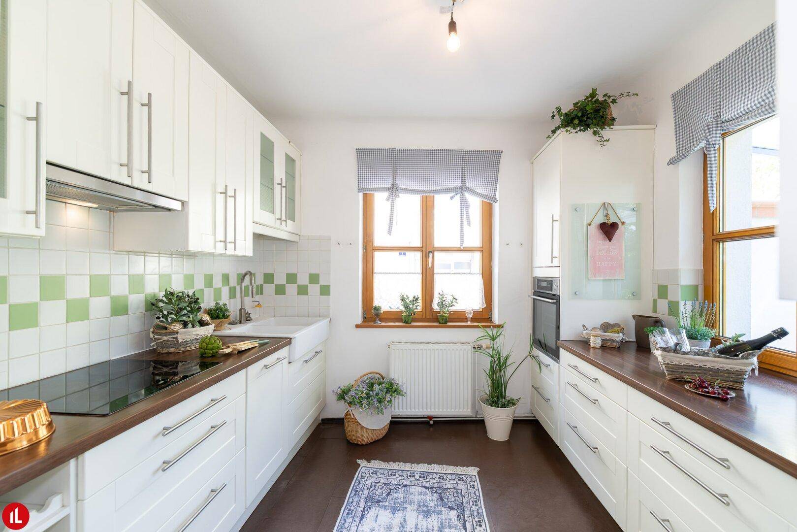 Helle Küche mit weißen Schränken, Holz-Arbeitsplatten und grün-weiß gefliestem Spritzschutz.