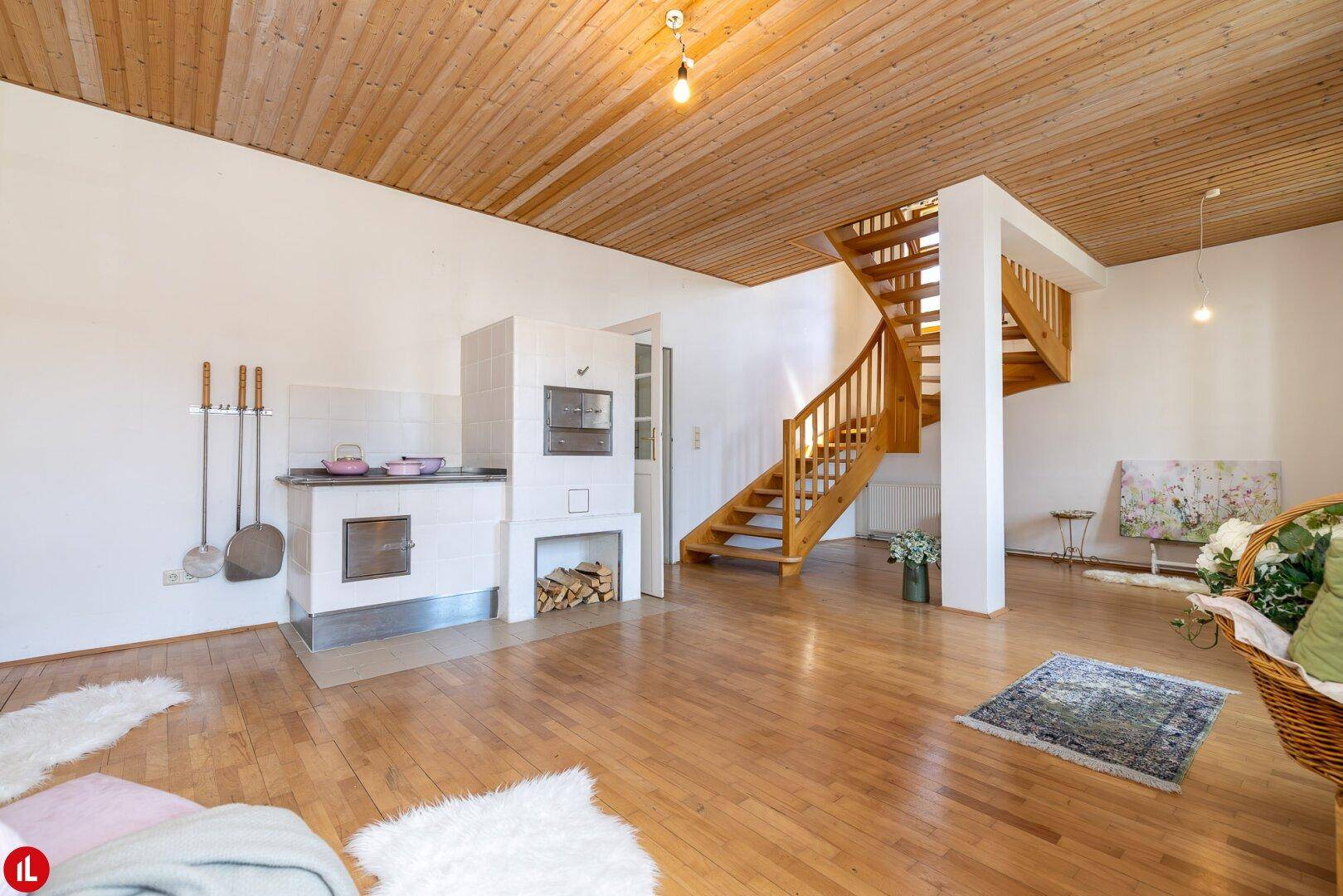 Gemütliches Wohnzimmer mit Holzboden, Holzdecke, Kachelofen und offener Holztreppe.