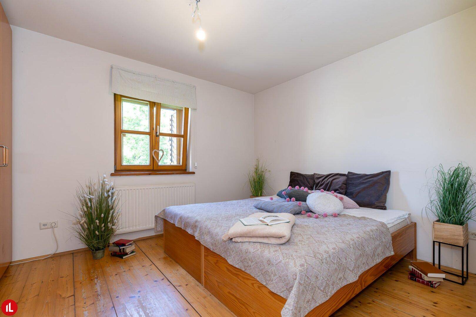 Helles Schlafzimmer mit Holzdielenboden, Fenster und schlichtem Doppelbett.