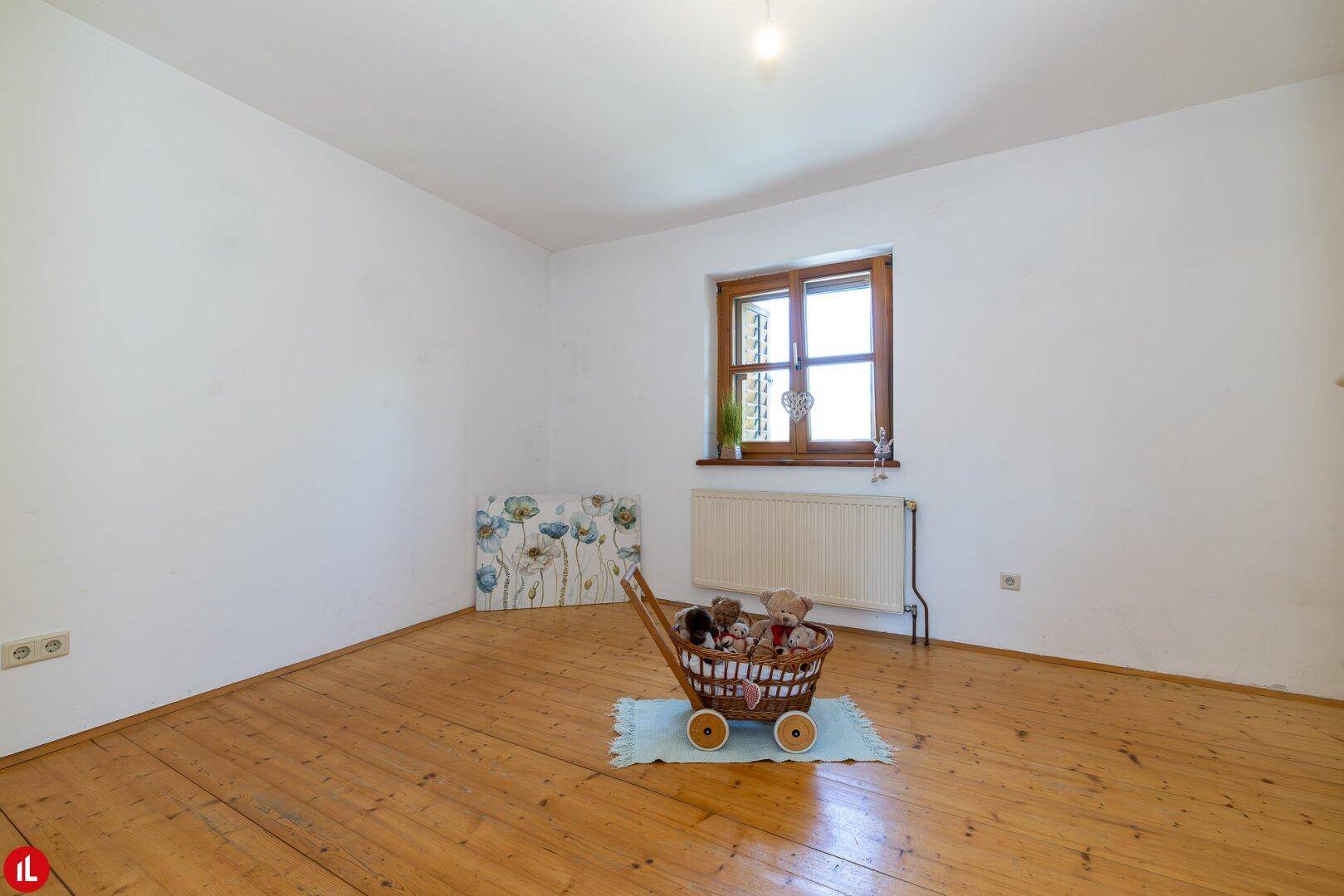 Freundliches Zimmer mit Holzdielenboden und Fenster, ideal als Kinder- oder Gästezimmer.