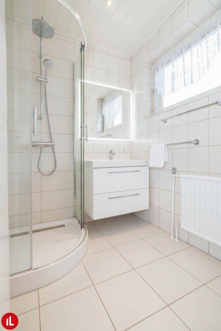 Modernisiertes Badezimmer mit Duschkabine, neuem Waschtisch und hellen Fliesen.