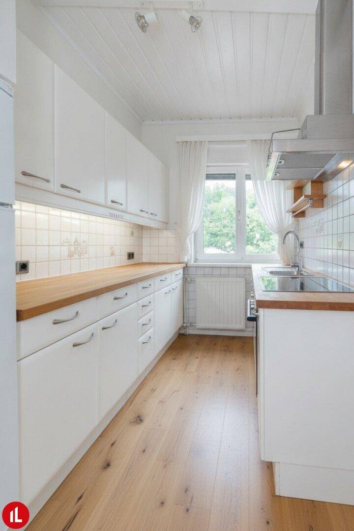 Helle Küche mit weißen Schränken, Holz-Arbeitsplatte und modernisiertem Boden.
