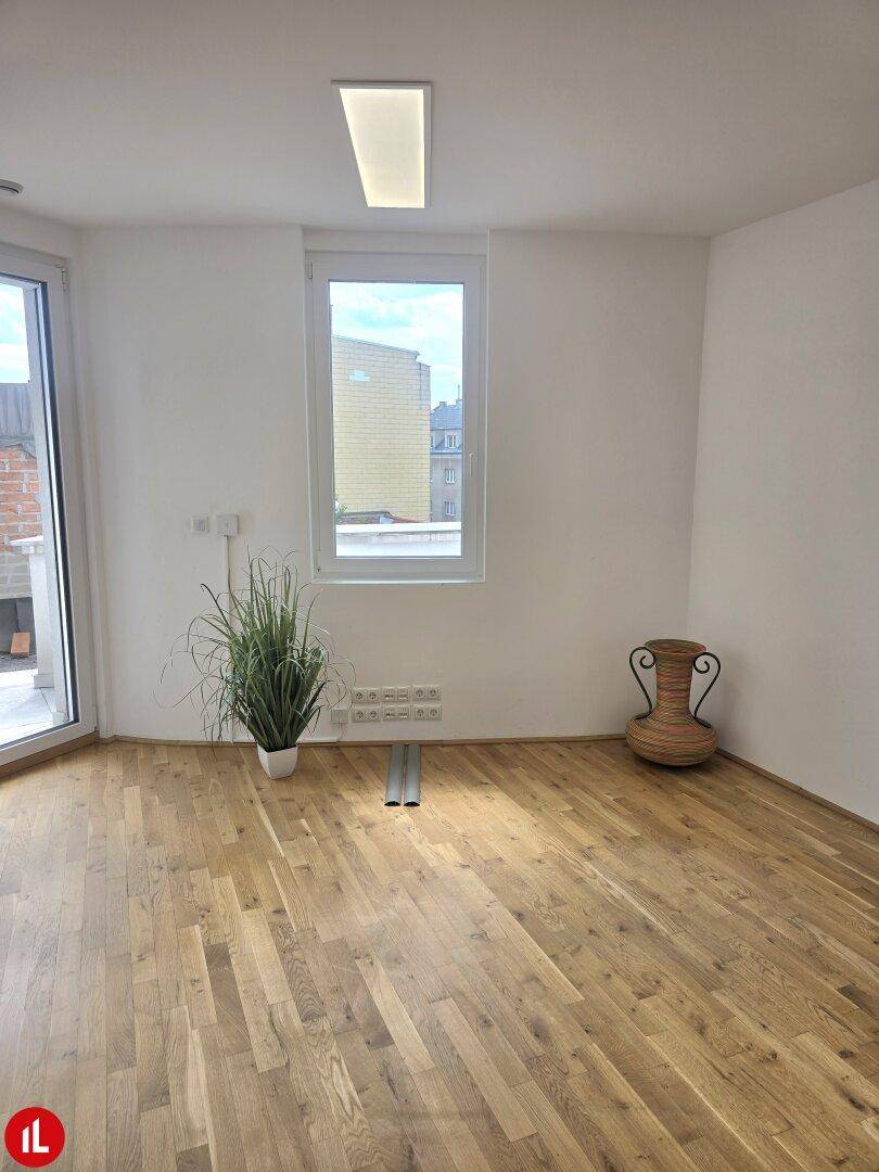 Heller Wohnraum mit Holzboden, großem Fenster und Zugang zu einem Außenbereich.