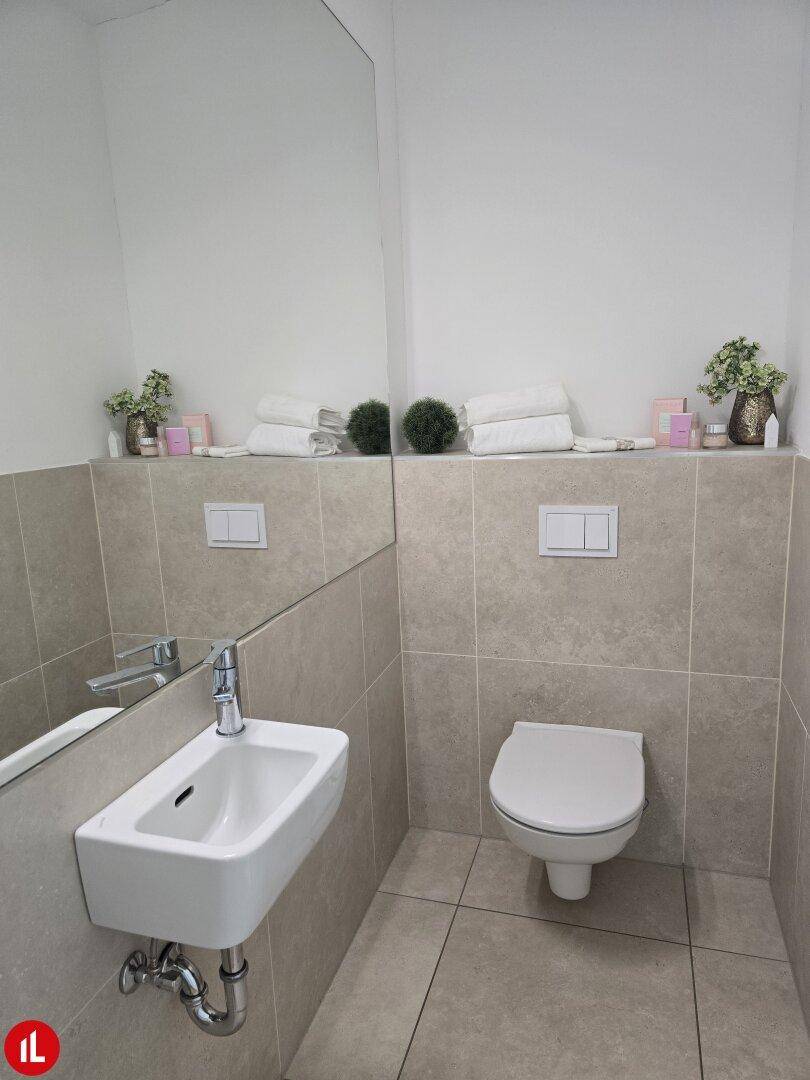 Modernes Gäste-WC mit Wand-WC, kleinem Waschbecken und hellen Fliesen.