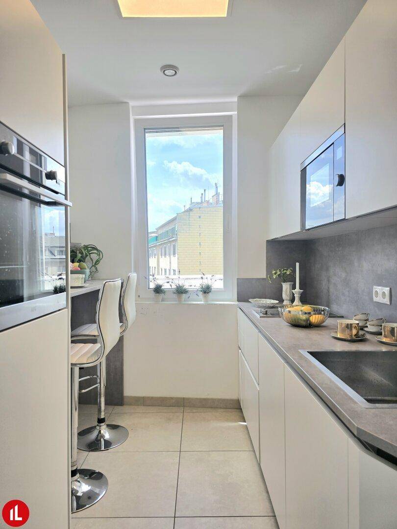 Moderne Küche mit weißen Schränken, integrierten Geräten und einer Frühstücksbar am Fenster.