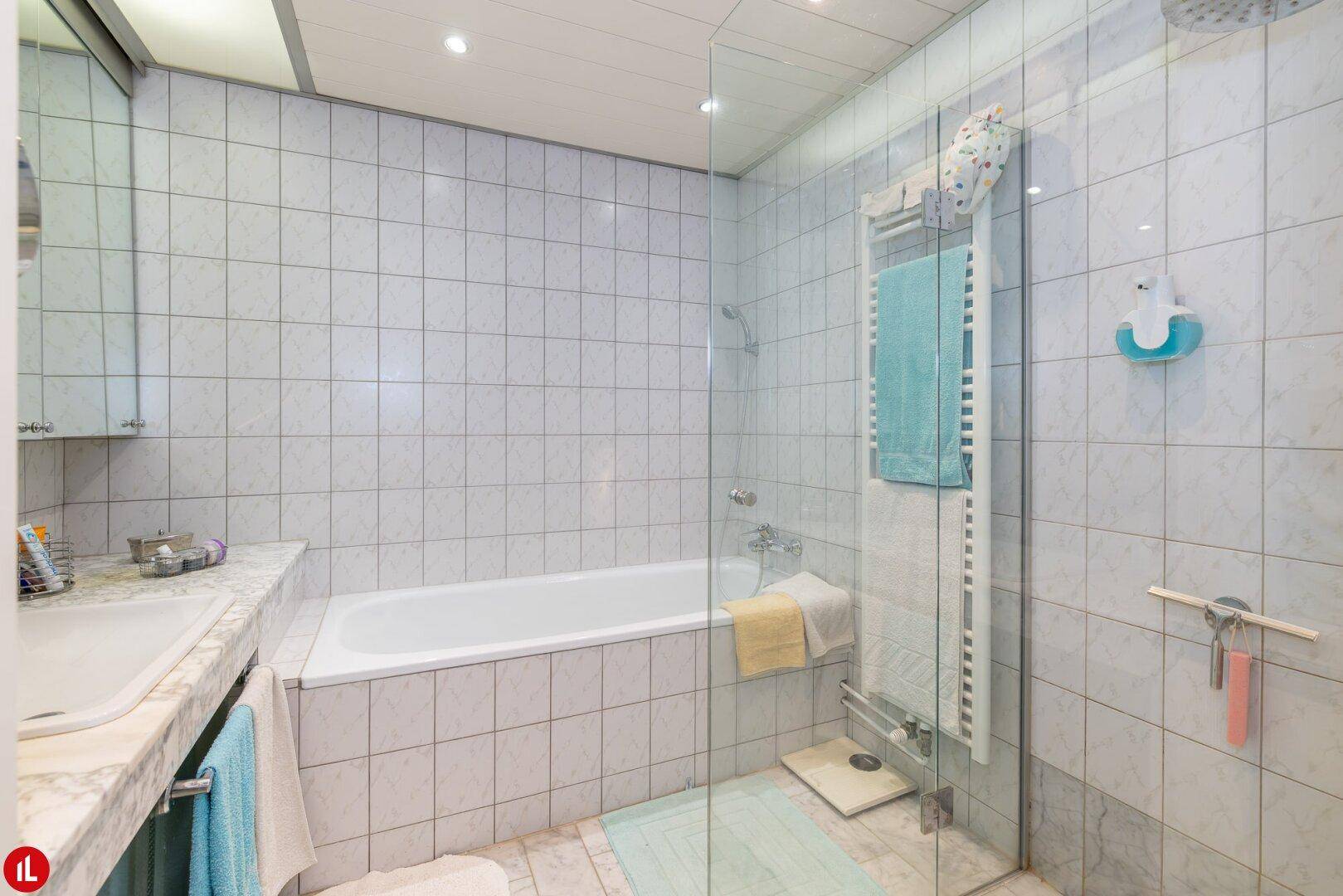 Badezimmer mit Badewanne, Duschkabine und hellen Fliesen, ausgestattet mit einem beheizten Handtuchhalter.