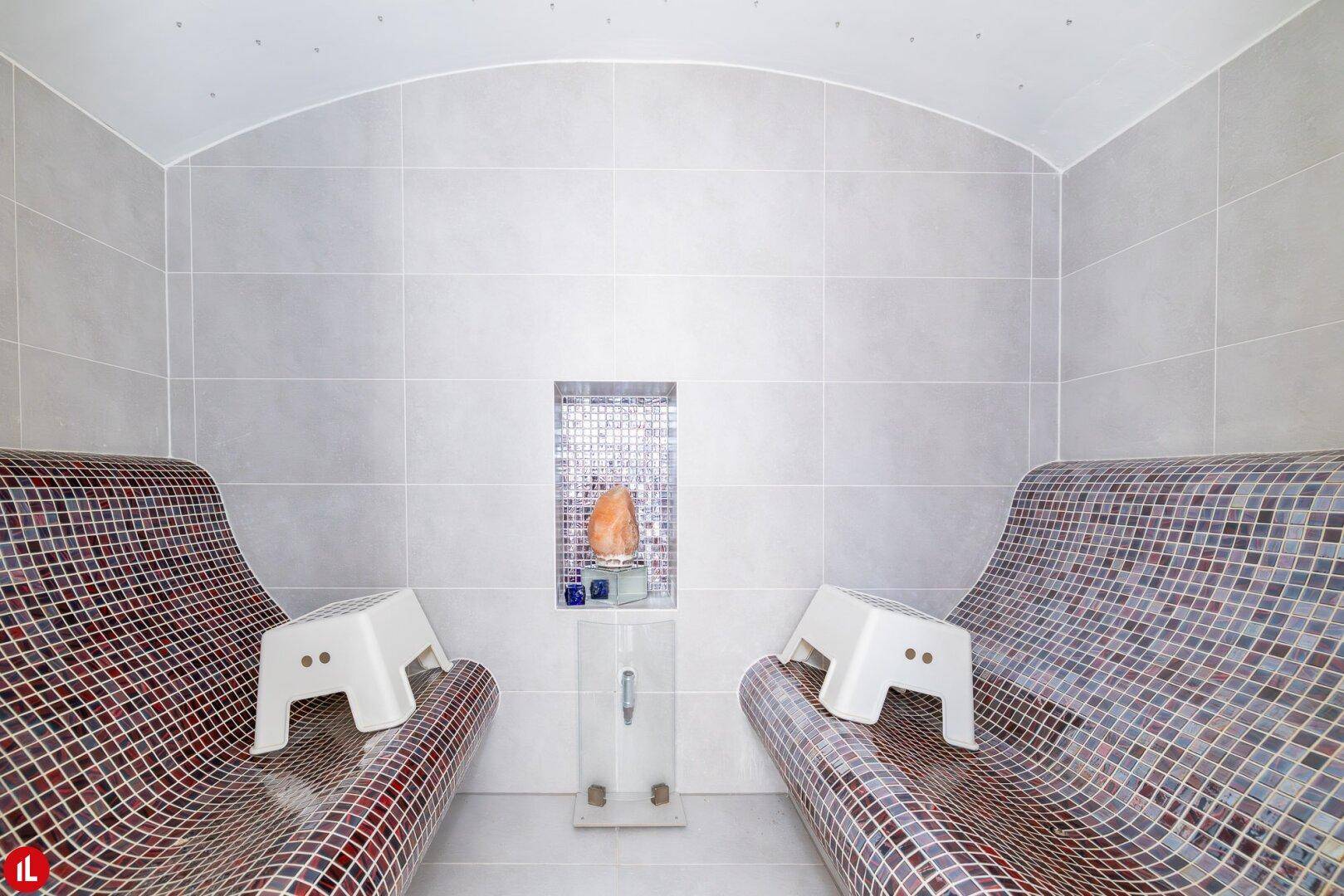 Entspannungsbereich mit beheizten Liegen und Mosaikfliesen, ideal für Wellnessanwendungen.