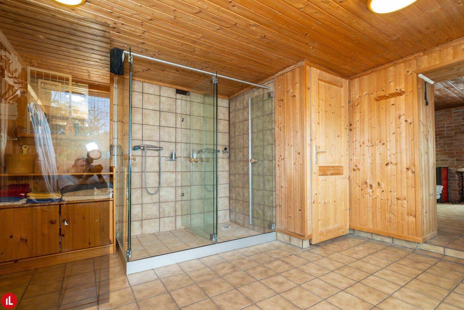 Große Duschkabine mit Glaswänden und Fliesenboden in einem holzvertäfelten Wellnessbereich.