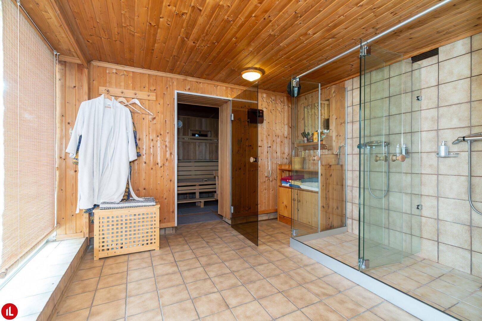 Wellnessbereich mit großer Duschkabine, Holzwänden und Zugang zu einer Sauna.