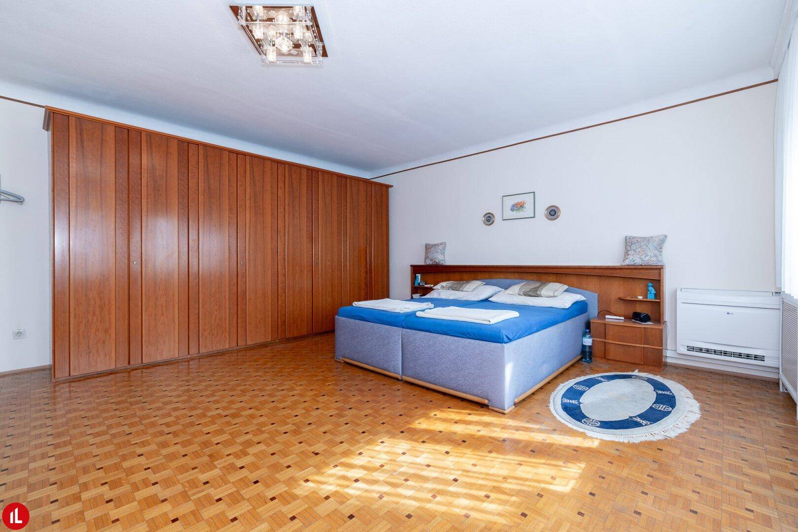 Geräumiges Schlafzimmer mit Parkettboden, Einbauschränken und einem Doppelbett.