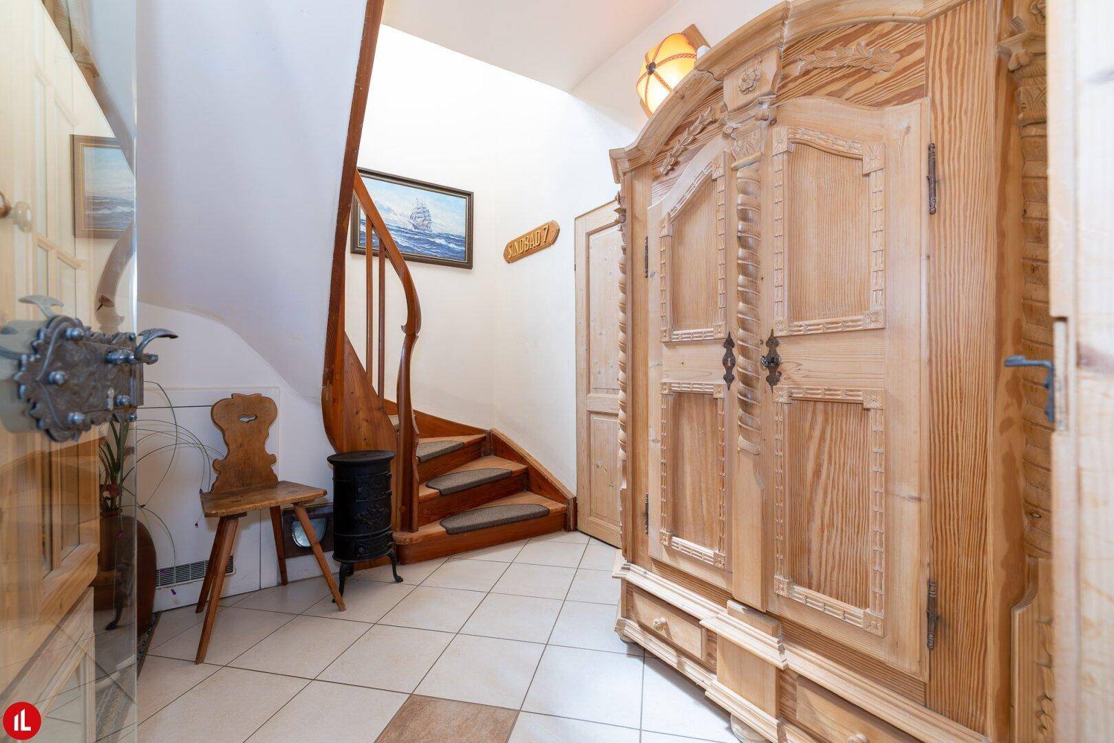Flur mit Holztreppe, Fliesenboden und einem großen, geschnitzten Holzschrank im Landhausstil.