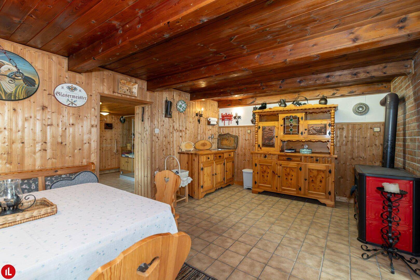 Rustikaler Kellerraum mit Holzwänden, Holzbalkendecke, Fliesenboden und einem Holzofen.