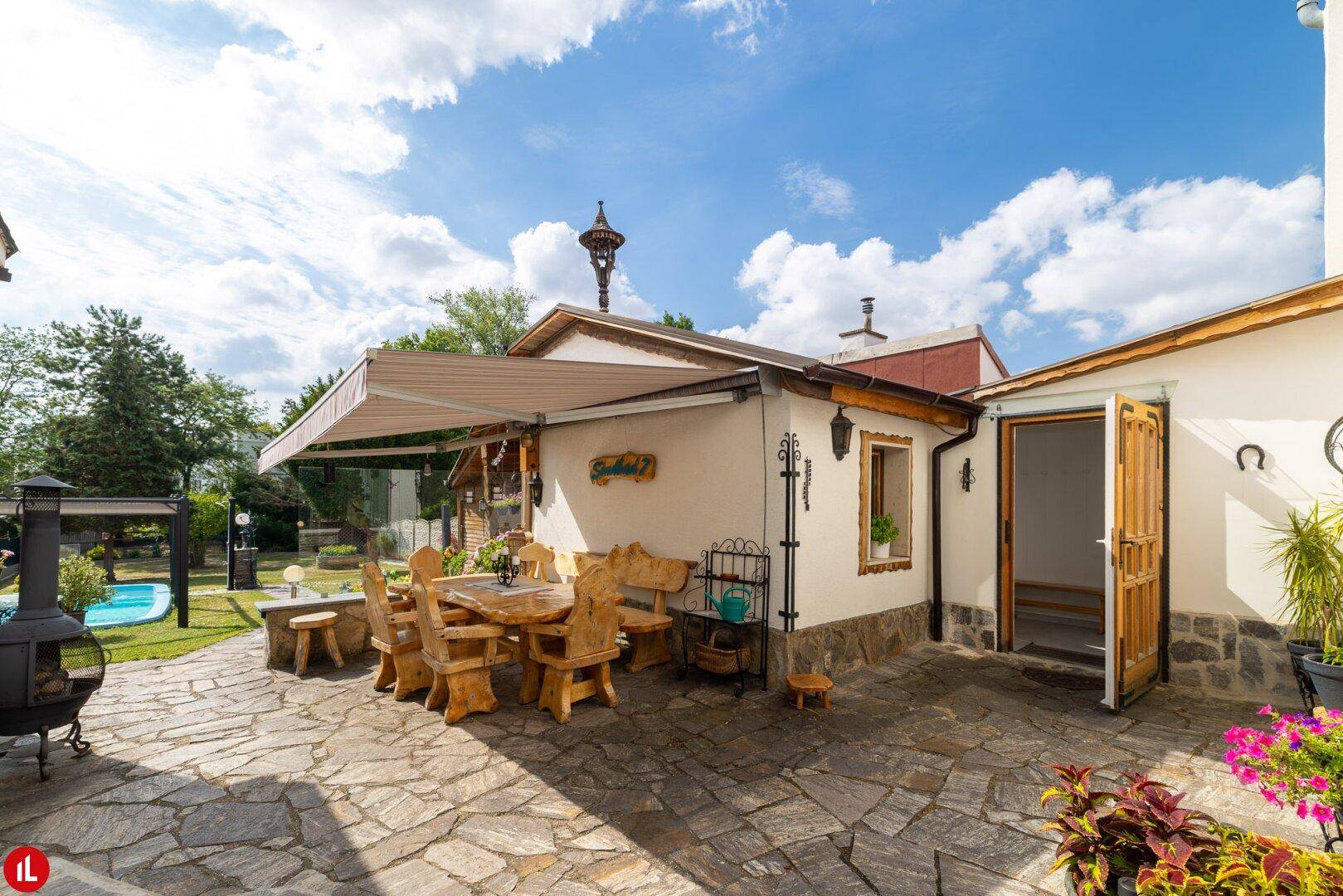 Gemütliche Terrasse mit rustikalen Holzmöbeln, Markise und Blick auf den Garten mit Pool.