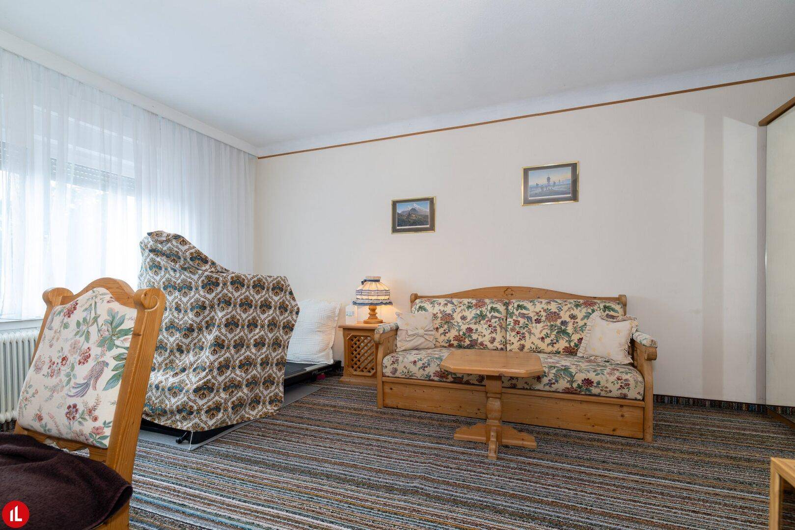 Helles Zimmer mit Teppichboden, einem Schlafsofa und traditionellen Holzmöbeln.