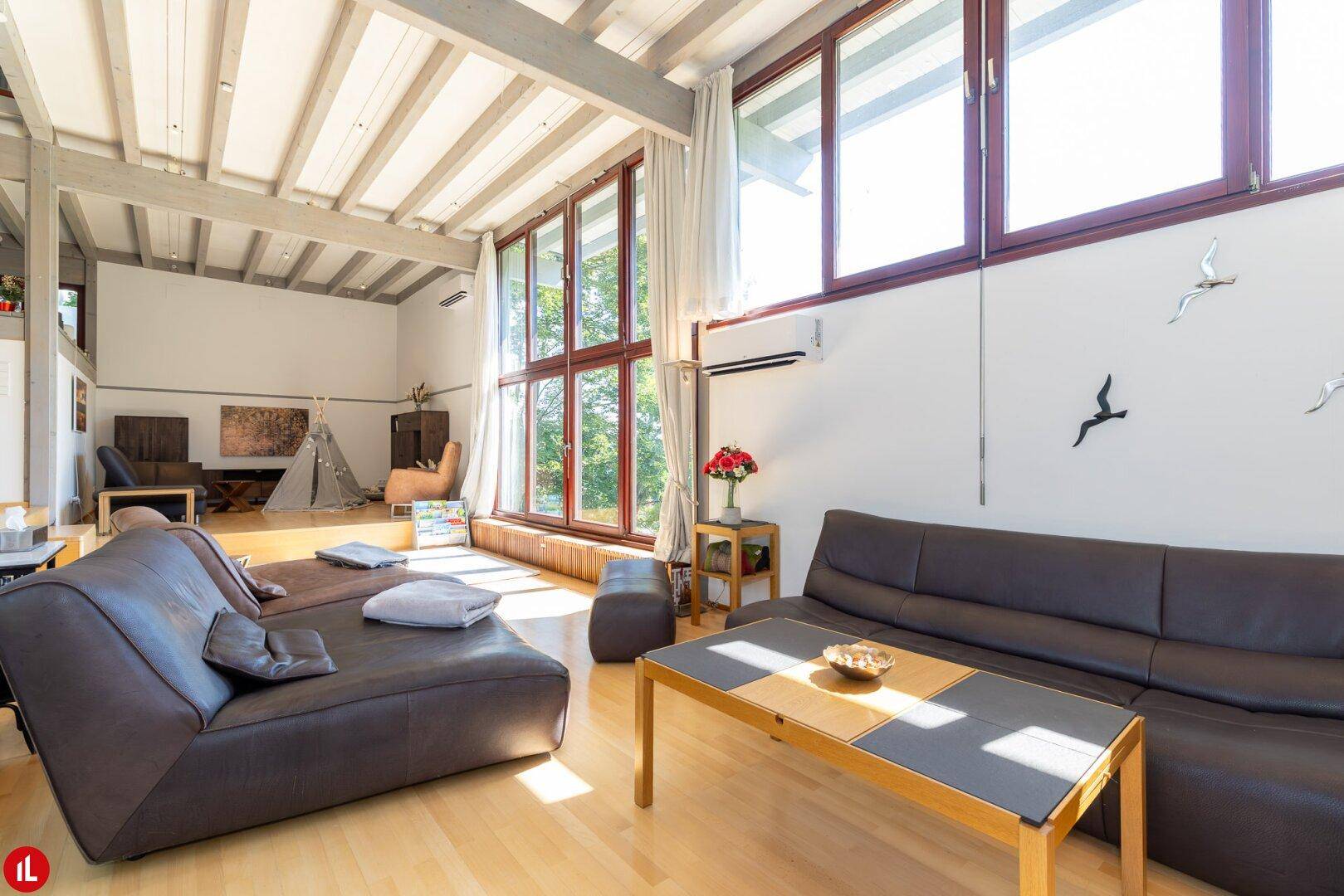Gemütliches Wohnzimmer mit bequemen Sofas, Holzbalkendecke und großen Fenstern.