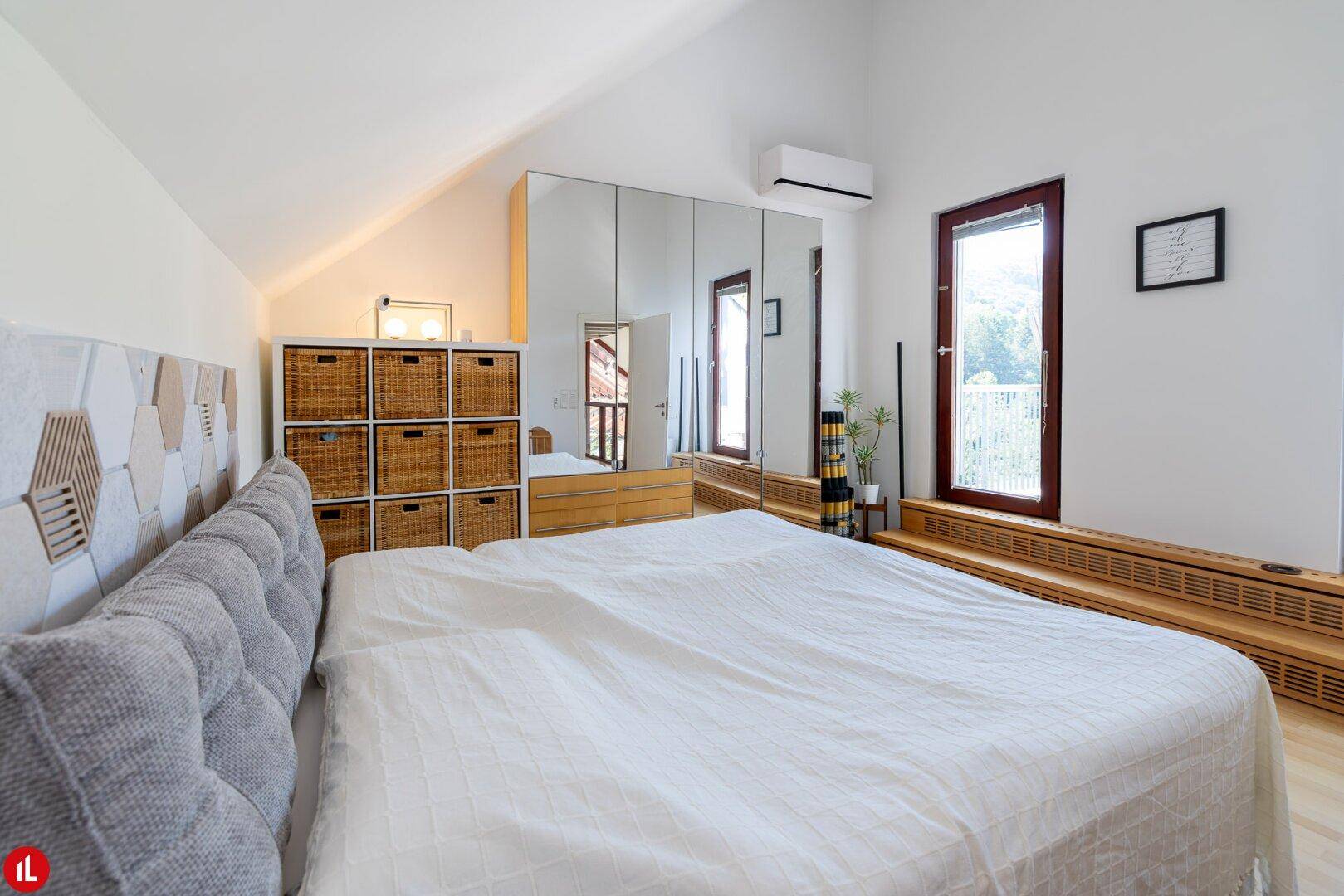Helles Schlafzimmer im Dachgeschoss mit Dachschräge, Spiegelschränken und Holzboden.
