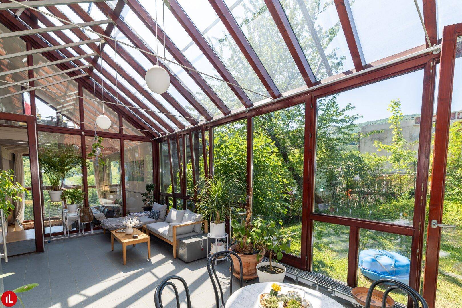 Geräumiger Wintergarten mit vielen Pflanzen, Sitzgelegenheiten und Zugang zum Garten.