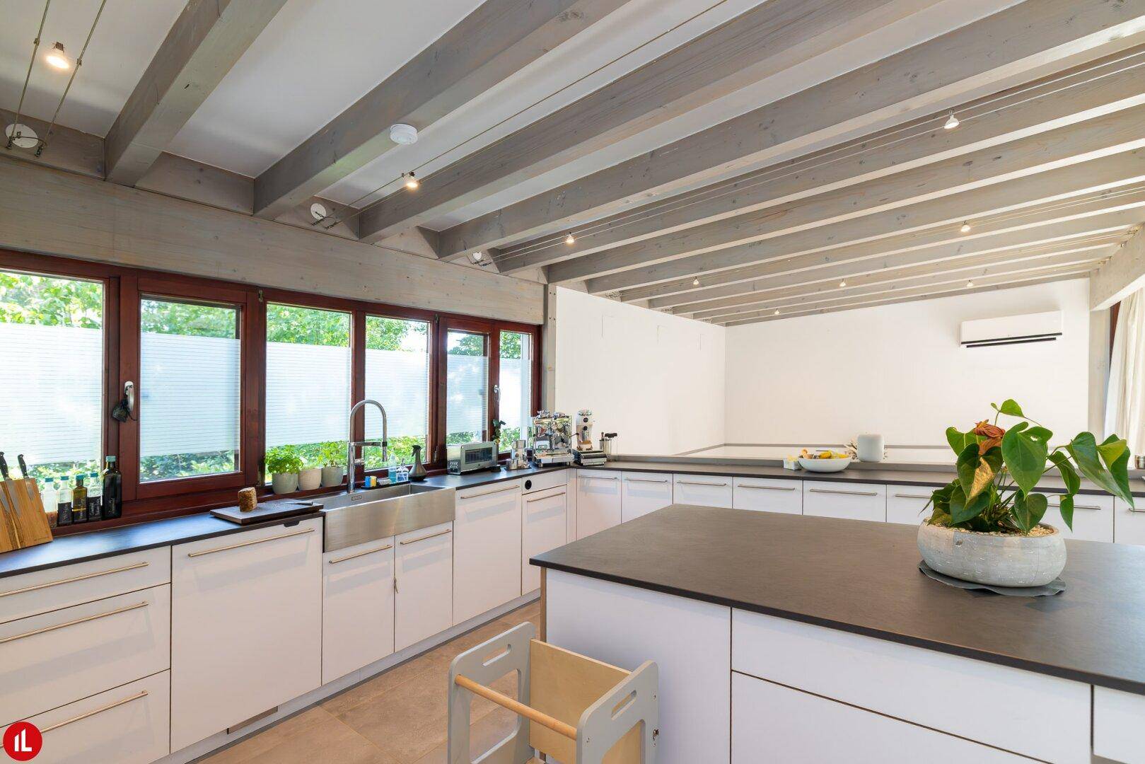 Moderne Küche mit weißen Schränken, dunkler Arbeitsplatte und Holzbalkendecke.
