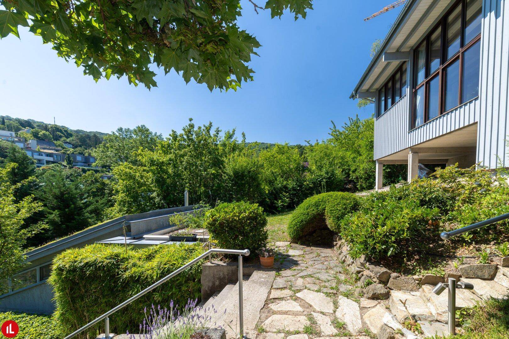 Steinweg führt durch den Garten zum modernen Haus, umgeben von üppigem Grün.