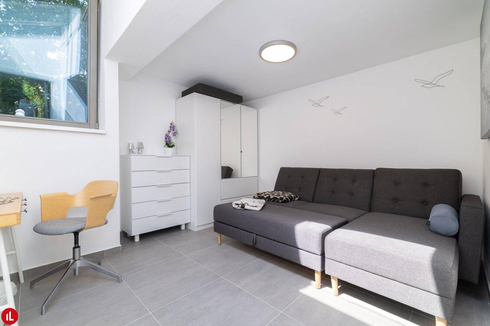 Gemütlicher Wohnbereich mit Sofa, Kommode und großem Fenster für viel Tageslicht.