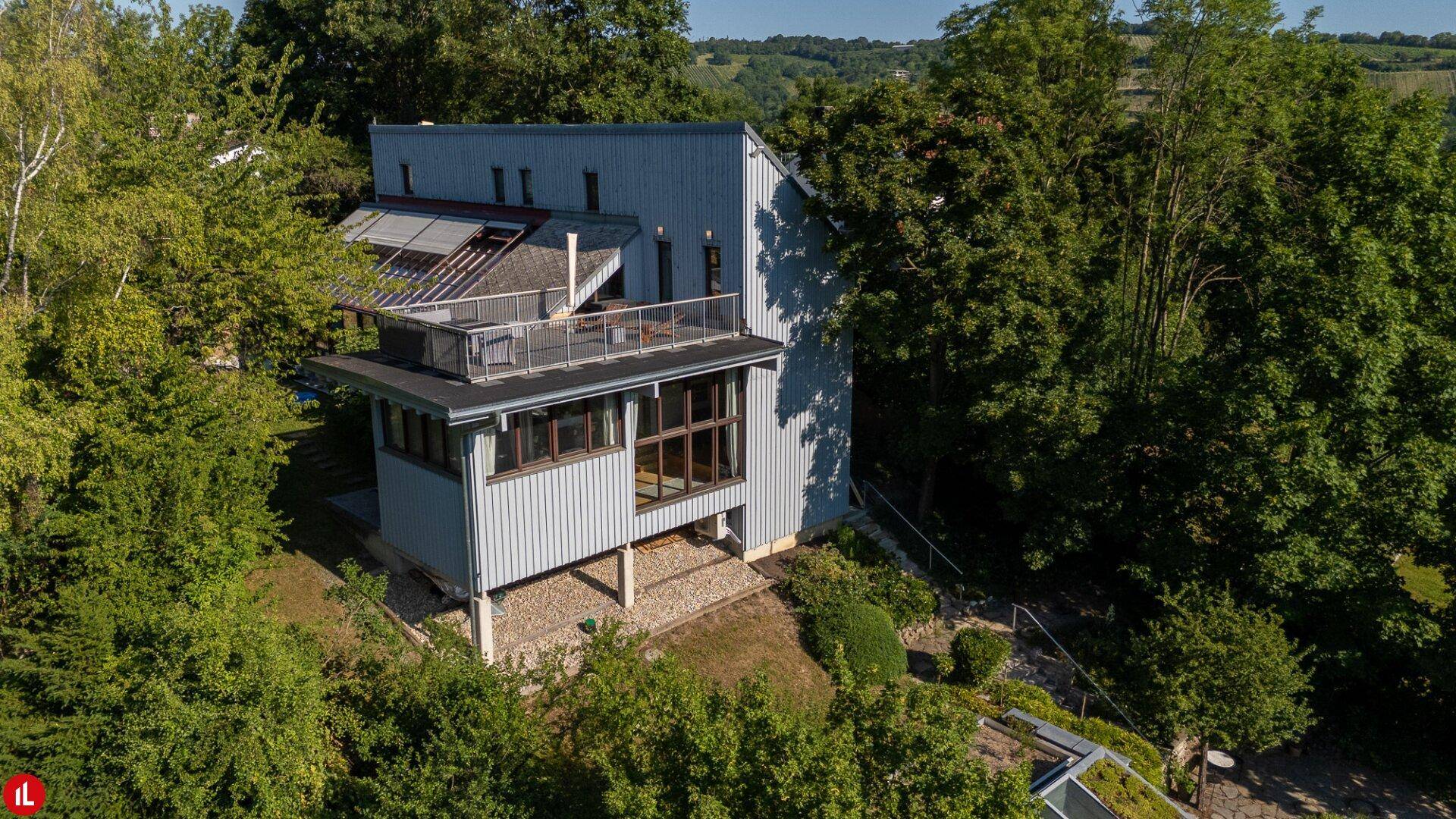 Luftaufnahme des modernen Hauses mit Dachterrasse, umgeben von Bäumen und Natur.