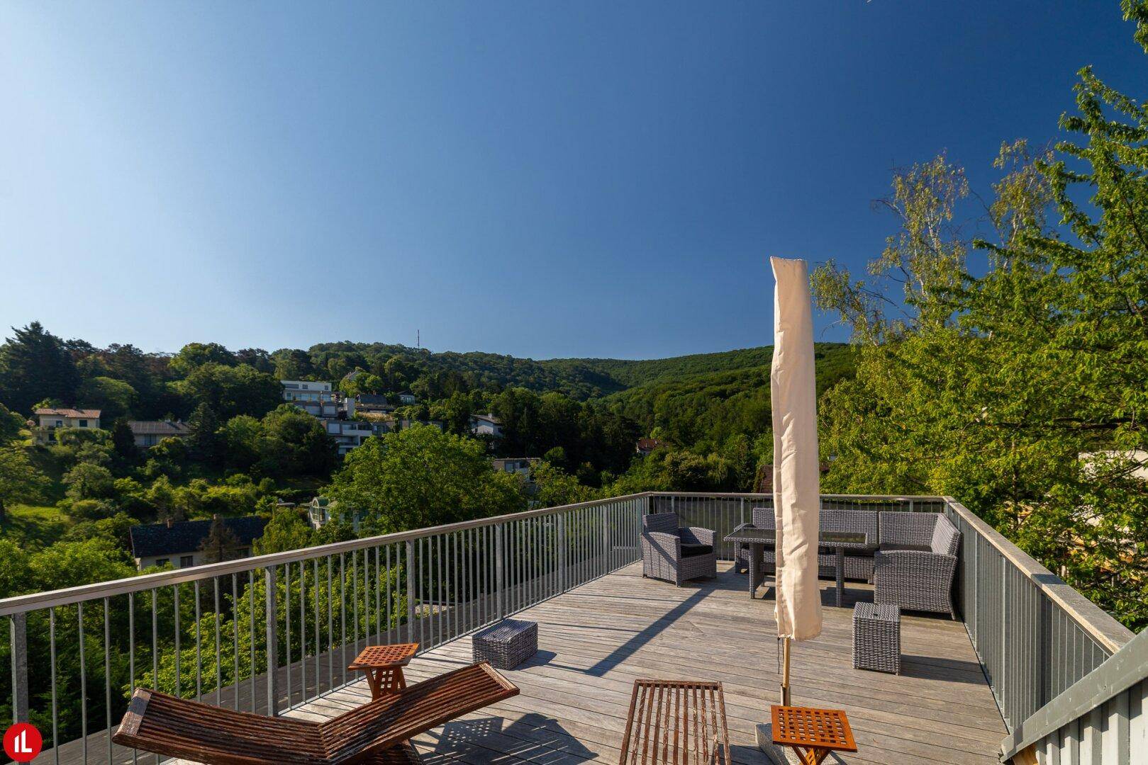Geräumige Holzterrasse mit Loungemöbeln und weitem Blick ins Grüne unter blauem Himmel.