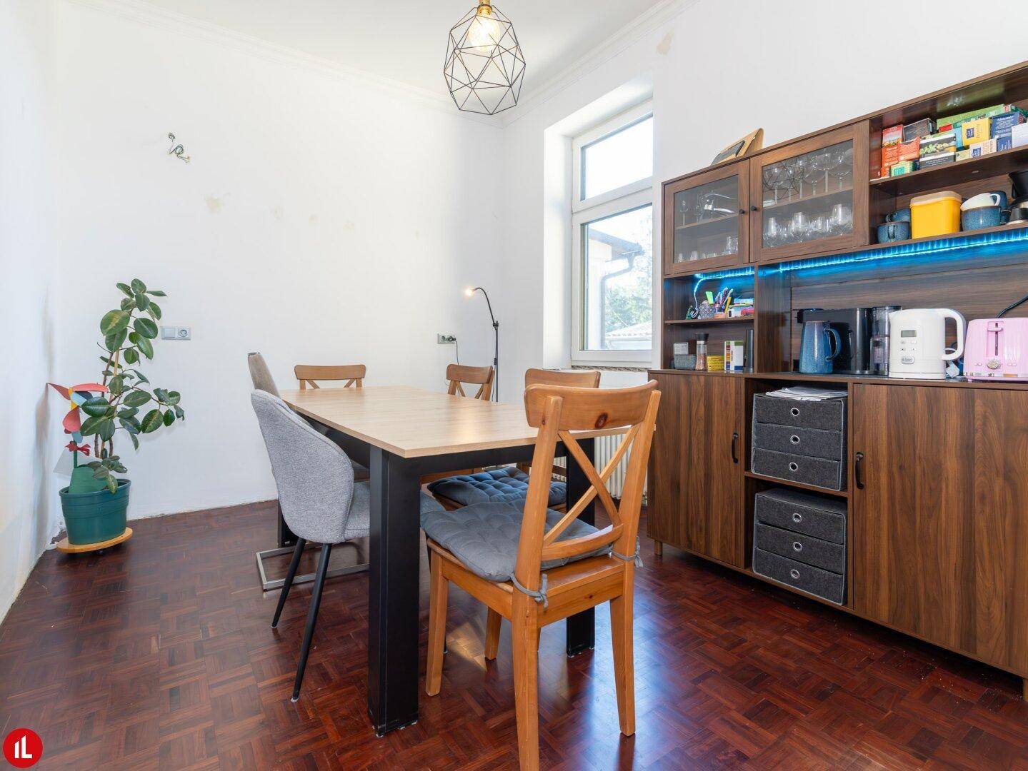 Esszimmer mit Holztisch, verschiedenen Stühlen und einem modernen Sideboard mit Beleuchtung.
