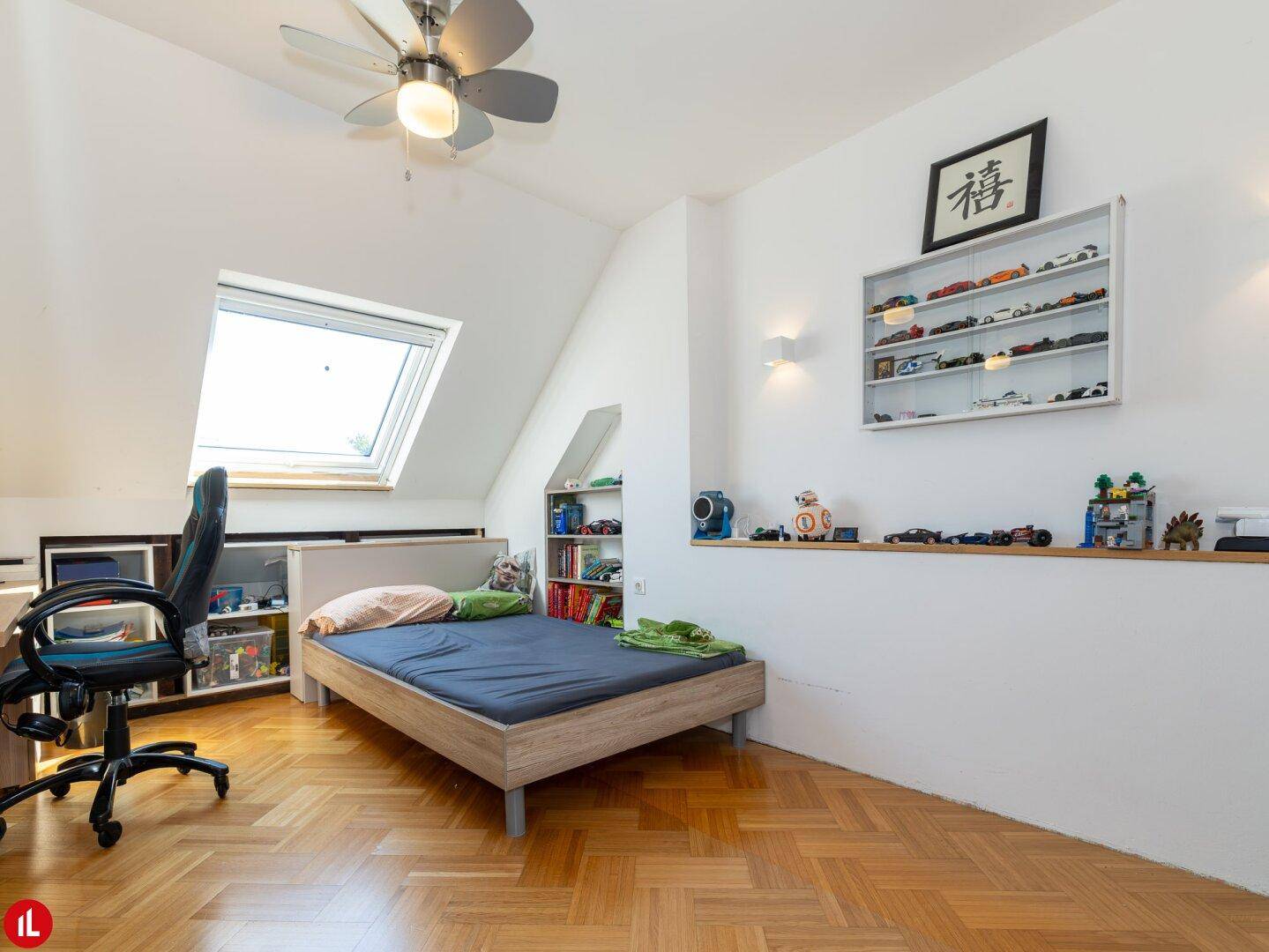 Kinderzimmer mit Einzelbett, Schreibtisch, Dachfenster und Spielzeugregalen unter der Schräge.