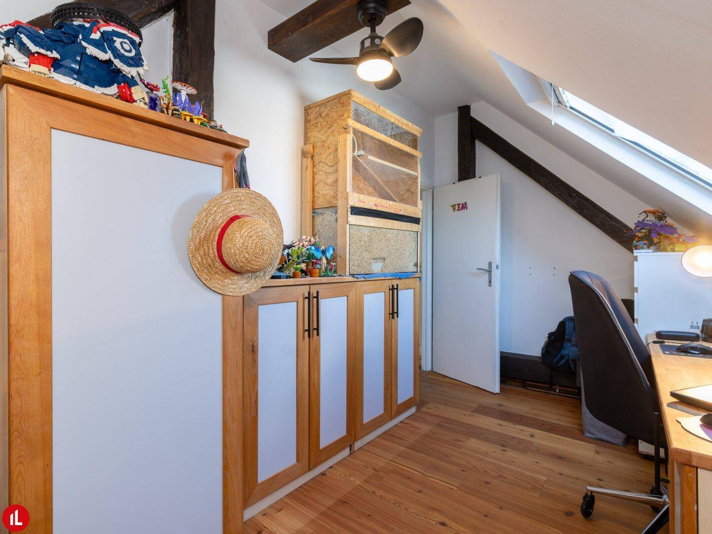 Arbeitszimmer mit maßgefertigten Holzschränken, sichtbaren Holzbalken und einem Dachfenster.