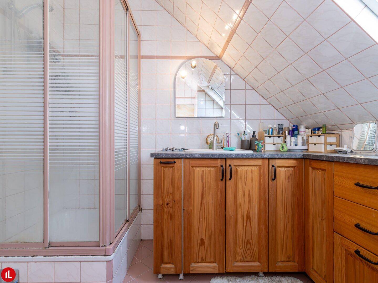 Badezimmer im Dachgeschoss mit Duschkabine, Holzwaschtisch und rosa-weißen Fliesen.