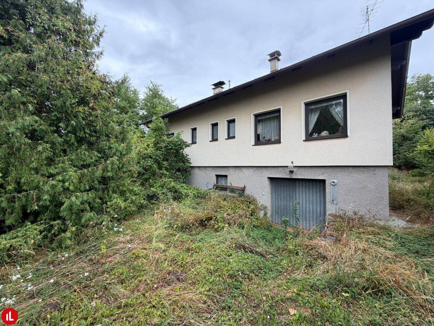 Seitenansicht des Hauses mit Garage und einem verwilderten Gartenbereich.
