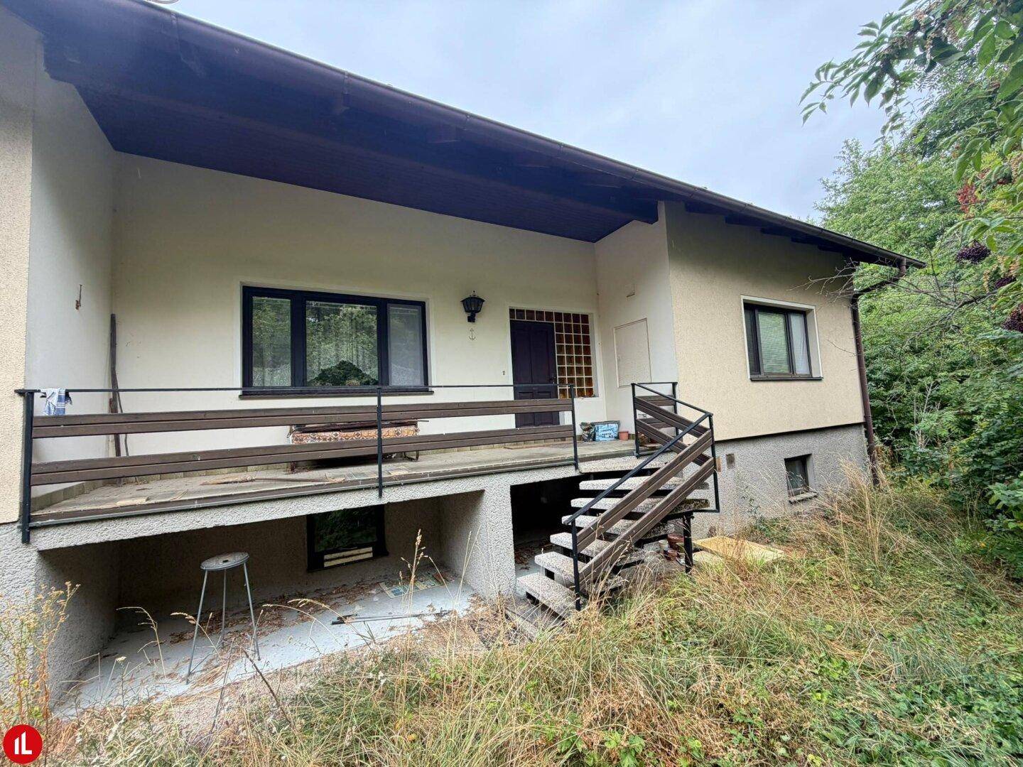 Rückseite des Hauses mit einem Balkon und Treppe, die zu einem verwilderten Bereich führt.