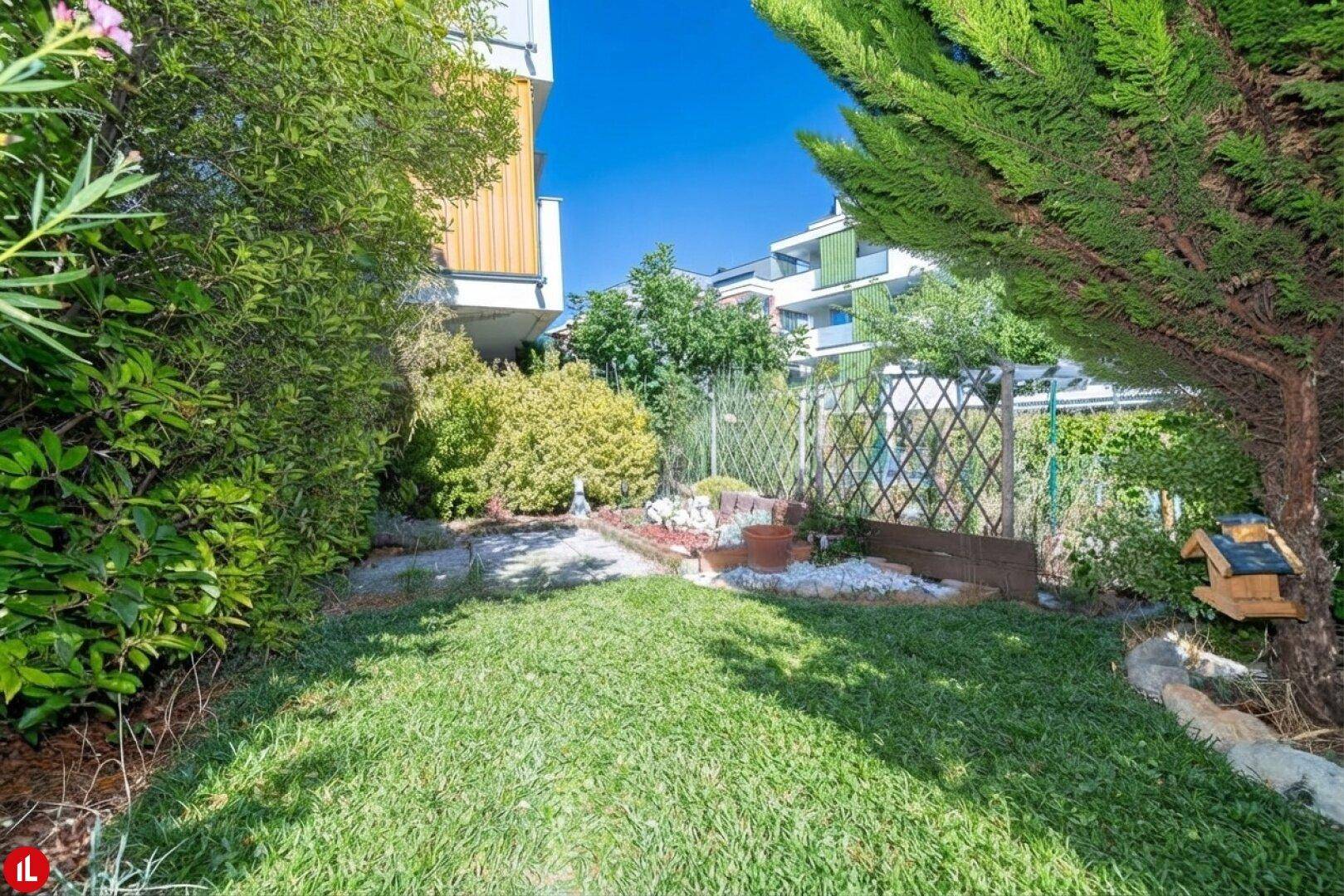 Gepflegter Gartenbereich mit Rasenfläche und üppiger Bepflanzung vor einem modernen Wohngebäude.