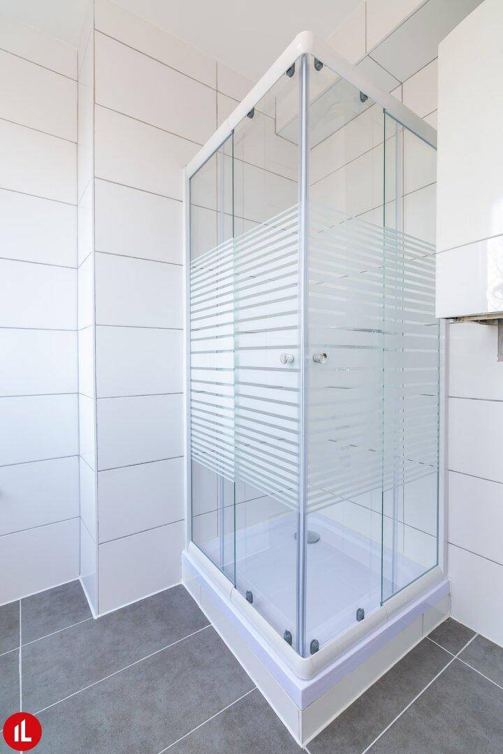 Modernes Badezimmer mit Duschkabine und hellen Fliesen an Wänden und Boden.