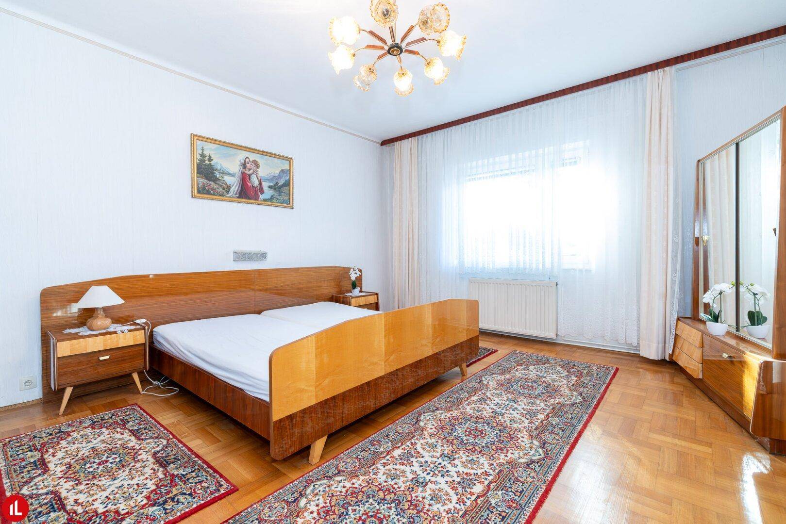 Schlafzimmer im traditionellen Stil mit Doppelbett, Holzmöbeln und Parkettboden.