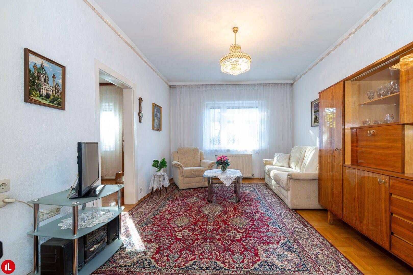 Gemütliches Wohnzimmer im traditionellen Stil mit Teppich, Holzmöbeln und viel Tageslicht.